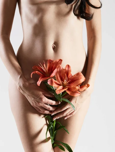 Intimate part of a womans body with flower in hands. Close up of a woman body with flower on her pubes. No retouch