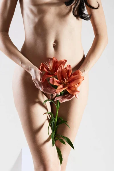 Intimate part of a womans body with flower in hands. Close up of a woman body with flower on her pubes. No retouch