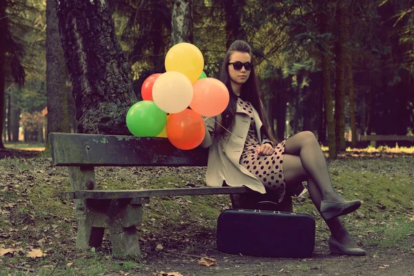 Menina bonita no parque com balões e uma mala — Fotografia de Stock