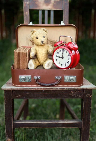 Back to school. Classic bell alarm clock, toy bear and old book in a vintage retro suitcase, bag.