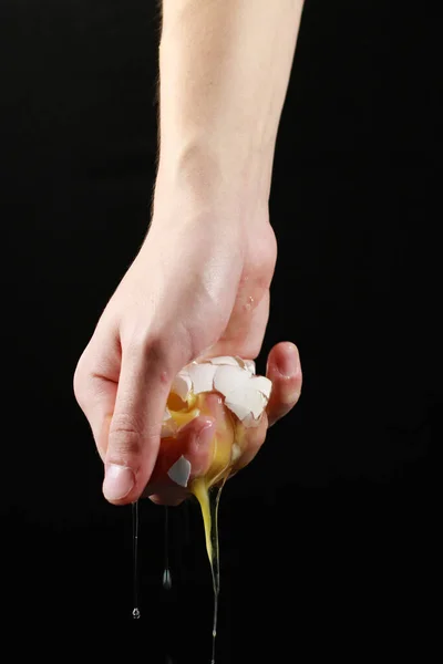 Bir eli siyah arka planda kırılmış yumurta.