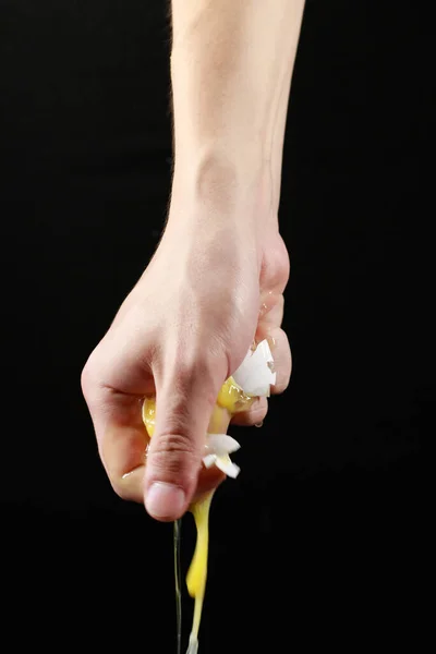 Kırık bir tavuk yumurtası siyah arka planda bir elden damlar.