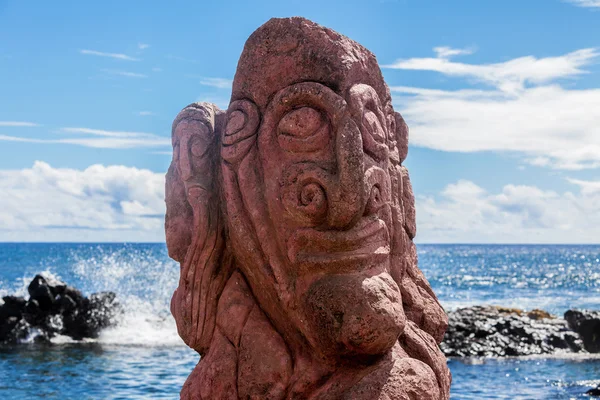Röd carving av ett ansikte på en moai på havsstranden — Stockfoto