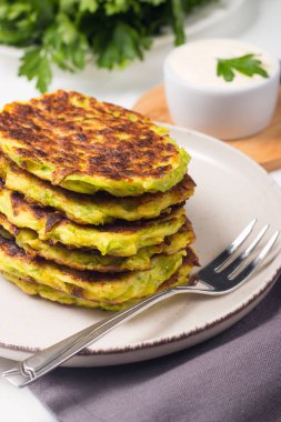Vegetarian zucchini fritters or courgettes pancakes, served with fresh herbs and sour cream.