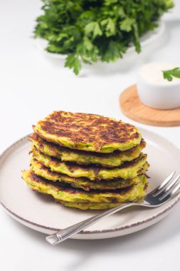 Vegetarian zucchini fritters or courgettes pancakes, served with fresh herbs and sour cream.