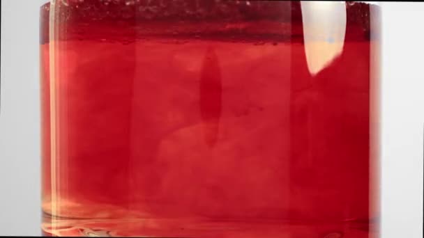 Red liquid poured into glass beaker of water, red blobs form and sink — Video Stock