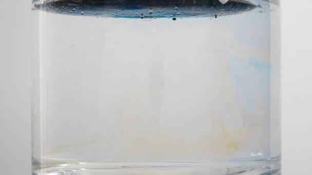 Drops of colorful ink swirl and expand through glass beaker of water — Stok video