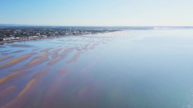 Exposed coastal sand flats at low tide with developed area and houses on shoreline, blue water and sunny sky, aerial. Location Sandgate, Queensland, Australia