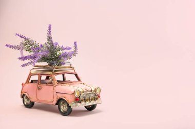 Pembe arka planda güller olan küçük pembe bir retro araba.