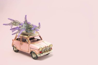 Pembe arka planda güller olan küçük pembe bir retro araba. 