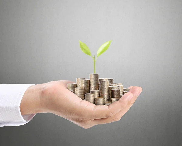 Empresario sosteniendo planta brotando de un puñado de monedas — Foto de Stock