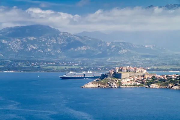 The citadel of Calvi with mountains behind and cruise liner in p — Stock Photo, Image