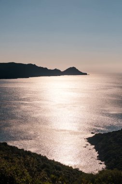 Korsika 'nın batı kıyısındaki Capu Rossu burnu Akdeniz' e karşı öğleden sonra güneş ışığında parıldıyordu.