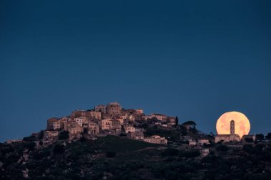 Korsika 'nın Balagen bölgesindeki Sant' Antonino antik dağ köyünün kilisesinin arkasından dolunay iniyor.