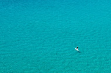 Ostriconi, Corsica, France - 12th July 2022. A standup paddle boarder with a child on board paddles across the translucent turquoise Mediterranean sea at Ostriconi in Corsica