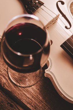 Bir bardak kırmızı şarap ve ahşap bir masada beyaz bir keman.      