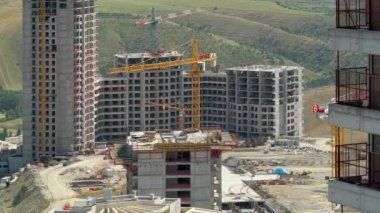 Cinematic 8K 7680x4320.Cranes and construction workers working at a major.Builders on building site.Transporting wall molds at skyscraper.Concrete and iron combination.Yellow crane mixed compex crowd.