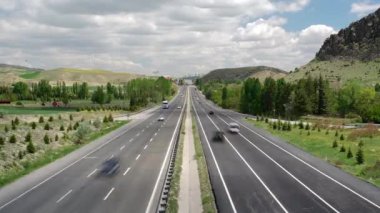 8K 7680X4320 4320p.Fast highway traffic in winding road.Highway traffic.Wide three lane road.Way surrounded by green trees.Heavy traffics.Overhead shot of cars, trucks on a major roads in countryside.