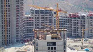 Cinematic 8K 7680x4320.Cranes and construction workers working at a major.Builders on building site.Transporting wall molds at skyscraper.Concrete and iron combination.Yellow crane mixed compex crowd.
