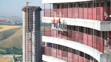 8K 7680x4320 4320p.Construction workers on a suspended platform on a skyscraper. Working in a hanging cradle at the construction site insulates the walls of the house insulation at the construction. Professional construction workers on the scaffold
