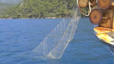Küçük balıkçı teknesinde ağ çekme ağı. Küçük plastik şamandıralara bağlı naylon balıkçı ağı. Eski teknede balık ağı makarası. Arka planda mavi okyanuslu küçük balıkçı teknesinde ağ ağ mekanizmasına yakın çekim. 