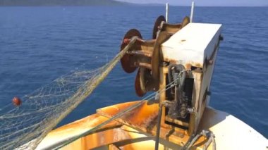 Küçük balıkçı teknesinde ağ çekme ağı. Küçük plastik şamandıralara bağlı naylon balıkçı ağı. Eski teknede balık ağı makarası. Arka planda mavi okyanuslu küçük balıkçı teknesinde ağ ağ mekanizmasına yakın çekim. 