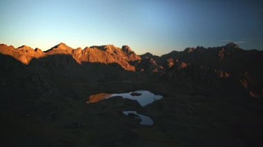 8K 7680x4320. Sabah gün doğumu ışıkları kayalık tepelere yansıyor. Yüksek irtifa dağ gölleri manzarası. Ağaçsız Alp Dağları 'ndan bir gün önce alacakaranlıkta gündoğumunun hızlandırılması.
