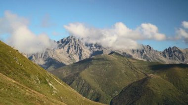 8K 7680x4320.Rocky dağı yüksek rakımlı tundra çayırlarının ardında yükseliyor. Zaman akıntılı bulutlar hareket ediyor. Yeşil çayırlar ve dik arazi. Manzaralı manzara yükseltisi mavi sonbahar tundrasını temizliyor..