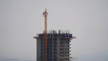 8K 7680x4320 Vinçler ve inşaat işçileri büyük bir binada çalışıyor. İnşaatçılar inşaat alanında. Gökdelende duvar kalıpları taşınıyor. Beton ve demir kombinasyonları..