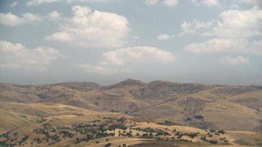8K 7680X4320 p.20 Standart bozkır arazisinde normal bir gün. Çorak çalılık, seyrek ağaçlı bozkır tepeleri. Ortam parçalı bulutlu ortam manzarası. Manzaralı hızlandırılmış sinematik manzara manzarası.