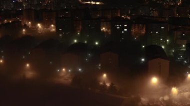 8K 7680x4320 4320p.Geceleyin şehirdeki evlerin arasında sis. Sisli hava. Sokak lambaları ve sislerdeki ev ışıkları..