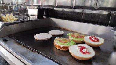 8K 7680x4320.Burgerciler hamburgercide pişiyor. Şef, şişko köftelerde çalışıyor. Caddelerin kenarındaki hamburgercide. Fast food restoranının tezgahı atölye eti, kızarmış patates yapıyor.