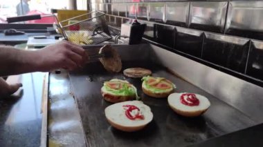 8K 7680x4320.Burgerciler hamburgercide pişiyor. Şef, şişko köftelerde çalışıyor. Caddelerin kenarındaki hamburgercide. Fast food restoranının tezgahı atölye eti, kızarmış patates yapıyor.