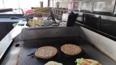 8K 7680x4320.Burgerciler hamburgercide pişiyor. Şef, şişko köftelerde çalışıyor. Caddelerin kenarındaki hamburgercide. Fast food restoranının tezgahı atölye eti, kızarmış patates yapıyor.