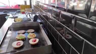 8K 7680x4320.Burgerciler hamburgercide pişiyor. Şef, şişko köftelerde çalışıyor. Caddelerin kenarındaki hamburgercide. Fast food restoranının tezgahı atölye eti, kızarmış patates yapıyor.