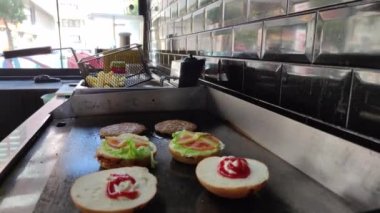 8K 7680x4320.Burgerciler hamburgercide pişiyor. Şef, şişko köftelerde çalışıyor. Caddelerin kenarındaki hamburgercide. Fast food restoranının tezgahı atölye eti, kızarmış patates yapıyor.