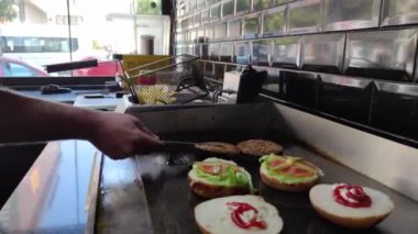 8K 7680x4320.Burgerciler hamburgercide pişiyor. Şef, şişko köftelerde çalışıyor. Caddelerin kenarındaki hamburgercide. Fast food restoranının tezgahı atölye eti, kızarmış patates yapıyor.