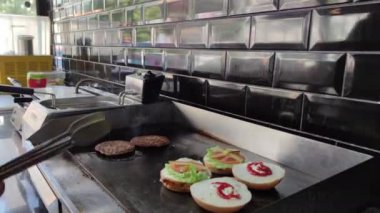 8K 7680x4320.Burgerciler hamburgercide pişiyor. Şef, şişko köftelerde çalışıyor. Caddelerin kenarındaki hamburgercide. Fast food restoranının tezgahı atölye eti, kızarmış patates yapıyor.