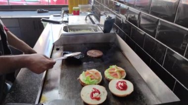 8K 7680x4320.Burgerciler hamburgercide pişiyor. Şef, şişko köftelerde çalışıyor. Caddelerin kenarındaki hamburgercide. Fast food restoranının tezgahı atölye eti, kızarmış patates yapıyor.