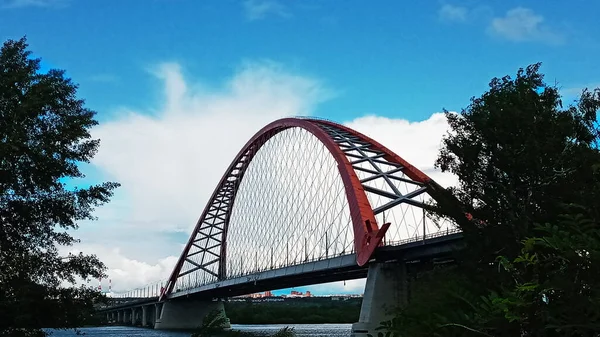 Czerwony łuk mostu linowego nad szeroką rzeką Ob. Nowosybirsk, Rosja. — Zdjęcie stockowe