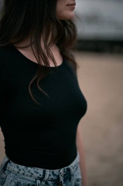 Kumsalda şehvetli ve muhteşem bir esmer. Sahilde sonbahar sezonu boyunca giyinik bir kadın. Siyah gömlek ve kot pantolon giyen kahverengi saçlı bir kızın portresi..