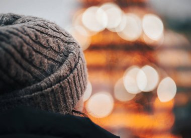 Arka planda gri şapkalı ve Noel dekorasyonlu genç bir kızın görüntüsü bulanıklaştı. Esmer kız, yeni yıl partisinden önce şehir merkezindeki kameraya dön.