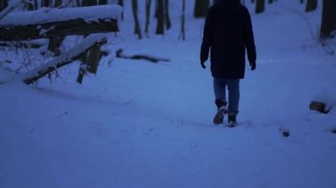 Walking in the snow. A shot of a woman looking back in the snowy woods. A girl walks slowly while wearing boots and a black jacket