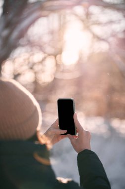 Cep telefonu genç bir kızda. Açık havada akıllı telefon kullanmanın bir maketi. Doğanın cep telefonuyla fotoğraflarını çekme kavramı.