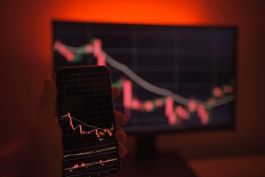 Cep telefonu ve bilgisayar ekranı şifreli para birimi grafiği gösteriyor. Çevrimiçi ticaret. Kırmızı arkaplanlı bitcoin döviz kuru kavramı