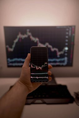 Arkaplanda bilgisayar ekranı olan şifreli döviz kurlarıyla akıllı telefon ekranı. Hisse senedi tüccarı, karlı fırsatları analiz ediyor. Bitcoin yatırıyor. Telefon ve bilgisayar kullanan kripto simsarı