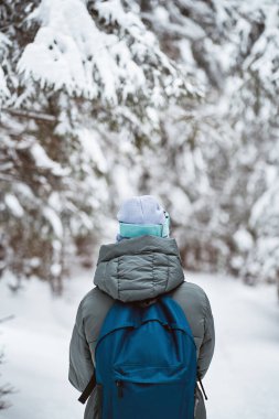 A person wearing a backpack in the snowy outdoor area. Back of the woman hiking. Concept of solitude adventures in winter mountains.