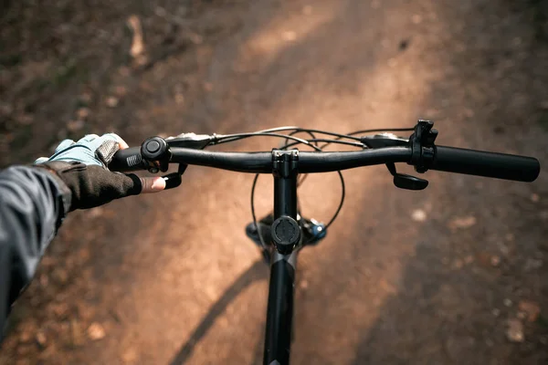 First-person view bicycle riding. Man riding a bike. holding bike handlebar with one hand in sport glove. Summertime outdoor leisure sport activity. Close up of bicycle handle bar