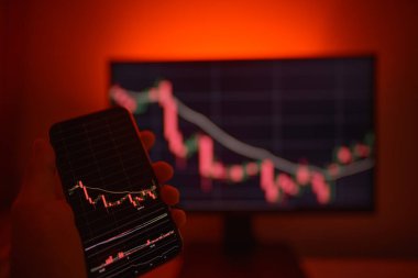 Cep telefonu ve bilgisayar ekranı şifreli para birimi grafiği gösteriyor. Çevrimiçi ticaret. Kırmızı arkaplanlı bitcoin döviz kuru kavramı