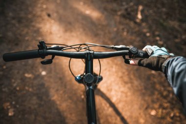 Şehirdeki orman yolunda güneş ışığına doğru bisikleti kullanmanın birinci şahıs görüntüsü. Bisikleti spor ve eğlence amaçlı kullanma kavramı..